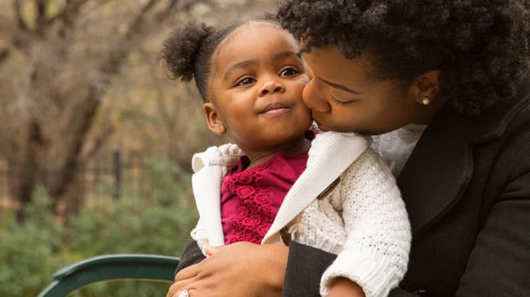 A mother kisses her toddler daughter on the cheek