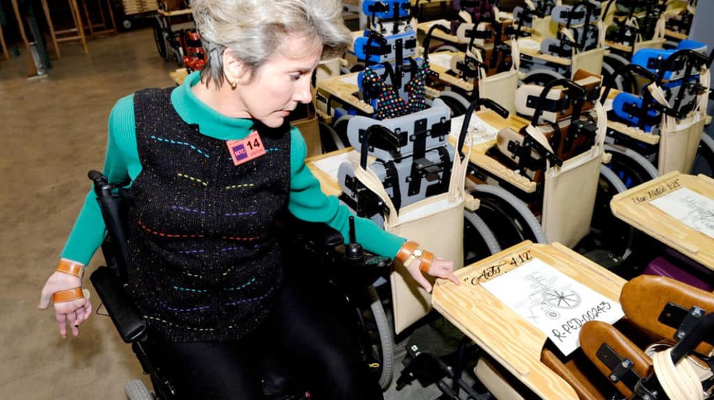 Joni in a classroom pointing to Acts 4:12 that is inscribed in a desk top