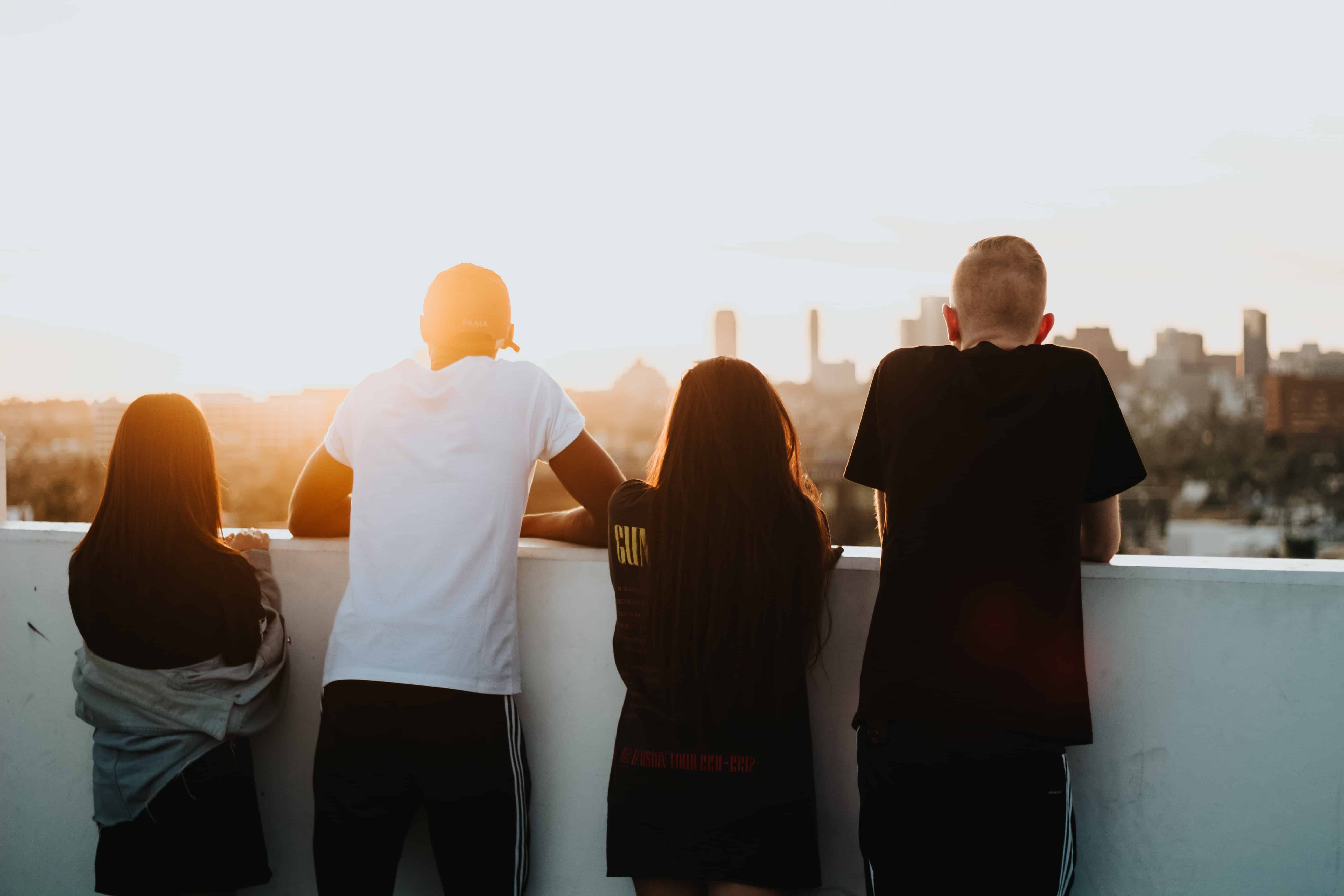 Family of all different ages leaning on a fence looking out at a beautiful sunset.