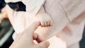 A man's fingers is grasped by the tiny hand of a baby.