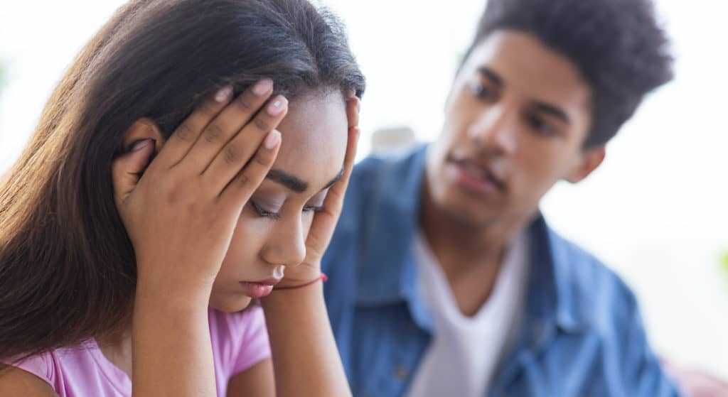 A young black man looks at his girlfriend thinking, "My Girlfriend is Pregnant? What Do I Do Now?"