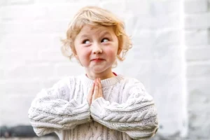 Little girl with blonde hair smiling with her hands in prayer