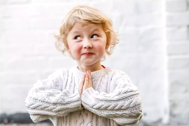 Little girl with blonde hair smiling with her hands in prayer