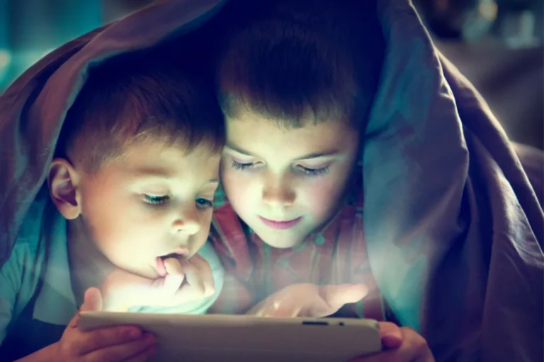 Two young boys under a blanket using a tablet, highlighting the importance of protecting children online.