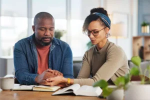 A couple prays together, holding hands at a table, symbolizing spiritual leadership, unity, and intimacy in their marriage.