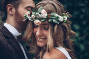 A man and a woman are standing together at their wedding. The woman is wearing a floral headpiece and a white dress, while the man is dressed in a dark suit.